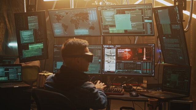 Cybercriminal in virtual reality glasses hacking and launching a nuclear missile by countdown using a computer with software in an illuminated modern hacker hideout