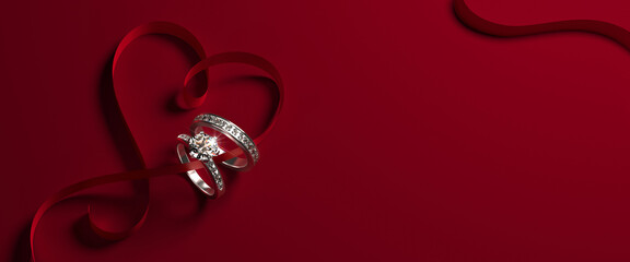 2 white gold engagement rings with diamonds and a heart-shaped ribbon on a red background. Romantic wedding jewelry background.