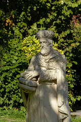 Stone sculpture of a saint holding bread, selective focus with green shurbs in the background, found in the beguinage of Antwerp, Flanders,s Belgium 