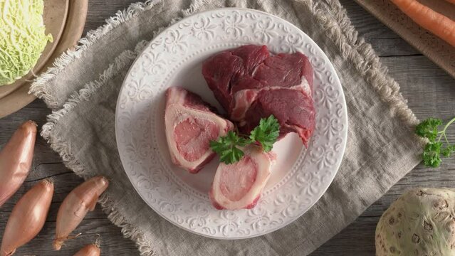 Female hands putting a plate with marrow bones and beef meat onto a table - ingredients to prepare bone broth or soup