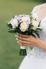 The bride's wedding bouquet of milk roses and lilac eustoms in the hands of the bride