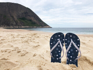Flip flops on the beach sand. Sea, sky and mountain ahead. Beach in Rio de Janeiro. - obrazy, fototapety, plakaty