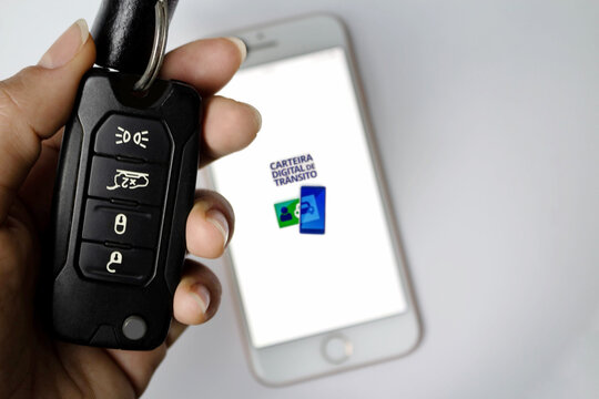 Person Holding Car Key And Digital Driver's License App In The Background.