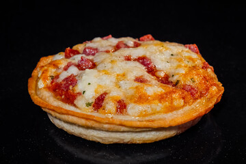 One mini pizza with ham, cheese baking on tray in electric oven, black background - close up view. Italian cuisine, homemade bakery, fast food, cooking concept