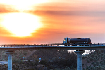 Tanker truck with dangerous goods circulating on a bridge at sunset.