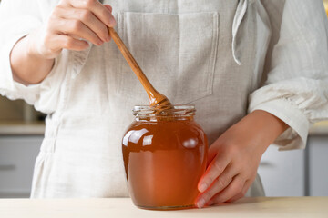 farmer pours a fresh harvest of honey into a glass jar. Organic Honey dripping, pouring from honey dipper in glasses bowl. Close-up 