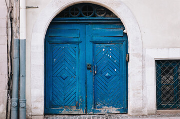 Old vintage closed wooden blue door with diamond-shaped pattern. Facade of gray stone in the form of an arch.