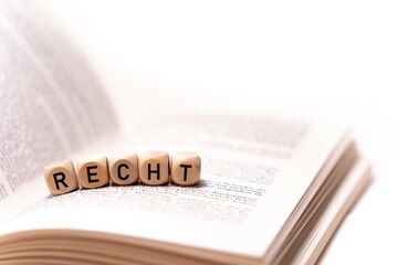 German word for law, RECHT, spelled with wooden letters wooden cube on a plain white background with a book, concept image