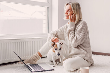 Happy middle aged woman with dog using her laptop at cozy white home