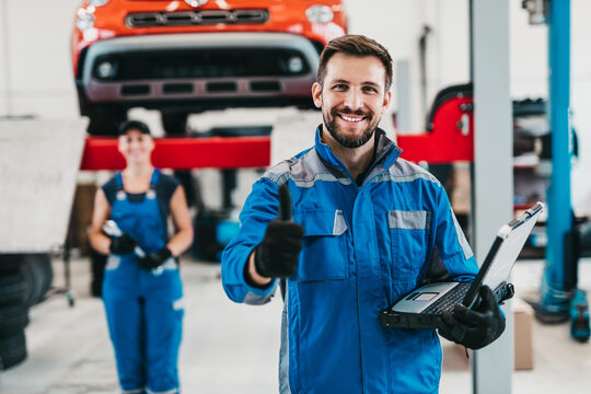 Male and female mechanics working together in large modern car repair service.