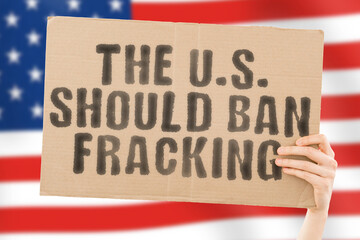 The phrase " The U.S. should ban fracking " on a banner in men's hand with blurred American flag on the background. Nature. Extract. Stop. Pipe. Energy. Drill. Raw. Power. Fuel. Fossil. Crisis. USA