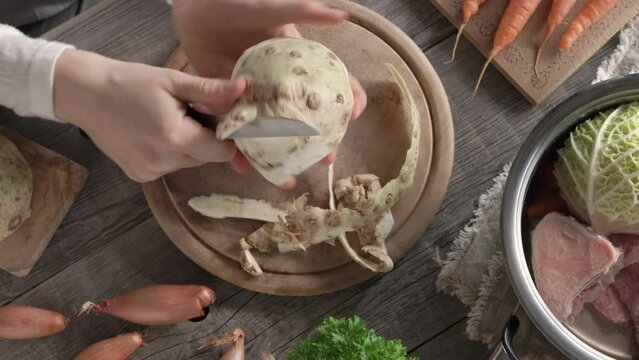 Peeling celery root and preparing homemade broth or soup from beef marrow bones and fresh vegetables