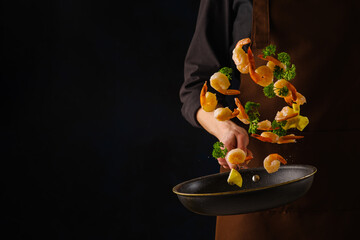 A professional chef cooks shrimp with herbs and lemon slices in a frying pan. Levitation. Black background. The concept is cooking seafood, healthy vegetarian food. Banner.