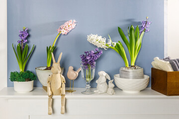 White hyacinth in large porcelain bowl, figurines of hares and a bird, are on the fireplace against the dark blue wall. Layout. Spring concept