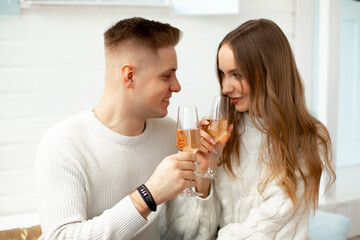 Young beautiful couple at home celebrates date of acquaintance, drinks wine from glass glasses. Romantic relationships. Love and tenderness. Beauty and youth.