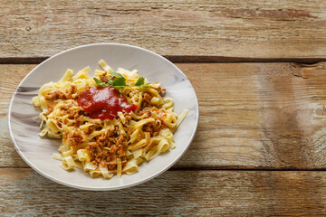 Pasta bolognese garnished with herbs and cheese in a plate on a wooden table. save a place.