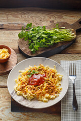 Pasta bolognese garnished with greens and cheese in a plate on a wooden table on a glossy board next to a fork and greens.