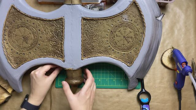 Girl decorates hatchet with string. Woman makes viking axe for cosplay festival. DIY celtic weapons in craft workshop.
