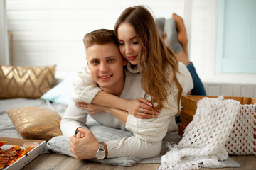 Portrait of young beautiful couple who arranged home date . Young woman hugs her lover, they are lying on floor on blanket in room. Creative date. Love and romance. 