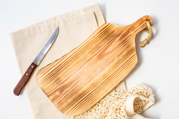 A cutting wooden board, a knife and linen towel are on a white background. Copy space. Thematic background for the recipe of the dish. Top view.