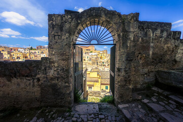 Open arched metal gate on medieval brick wall with view over old town at Matera