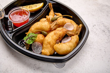 Macro selective focus tempura shrimp with sweet sour chili sauce and radishes in black plastic container on light background