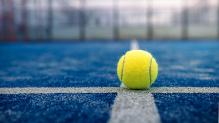 Yellow ball on floor behind paddle net in blue court outdoors. Padel tennis