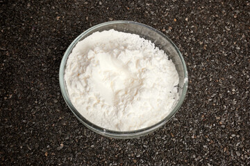 Cocaine powder in Petri dish on ruberoid textured surface. Dark gray textured background. Dark business of narcotic dealers. Chemical glassware with heroin flour. Toxic dust inside chemical dish.