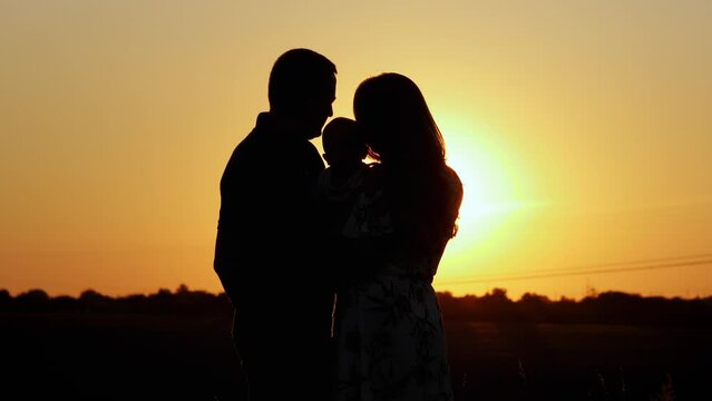 Unrecognizable silhouette of family at sunset, parents hug and kiss their child, family values and parental love