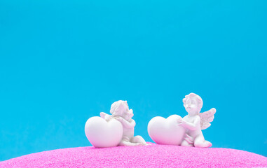 Angels with heart on pink sand and blue background. Minimal background concept. Love is in the air.