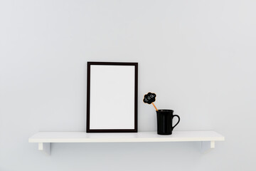 A black frame stands on a white shelf next to a black cup.