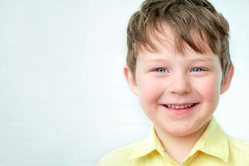 portrait of a happy, smiling blue-eyed boy 4-5 years old. A child on a light background in a yellow shirt. horizontal photo.