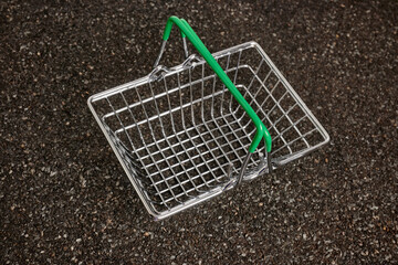 Metal shopping basket on ruberoid textured surface. Black textured background. Metallic mesh...