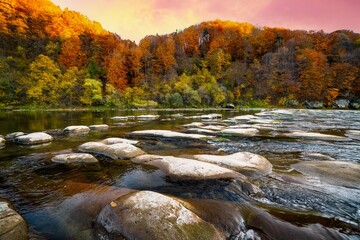 Stone bank against colorful trees growing on hills in autumn