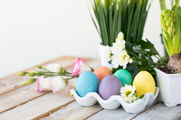 Easter composition, holiday home decor. Colourful eggs, flowers on the white wooden table. Copy space for text