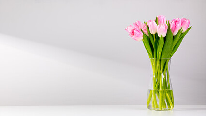Pink tulips in a vase on a white table - obrazy, fototapety, plakaty