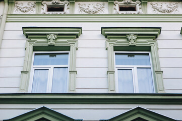 Two green windows with wooden frames and embossed edging. Neoclassical complex building, facade of an old house in Lviv, Ukraine.