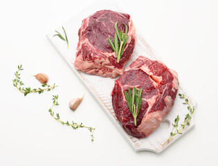 raw piece of beef ribeye with rosemary, thyme on a white table, top view