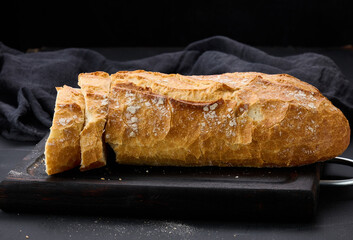 baked whole oval bread made from white wheat flour on a black table, fresh pastries