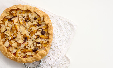 baked round pie with apple pieces, sprinkled with almond flakes on a white table