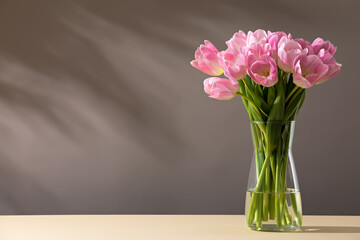 Pink tulips in a vase on a table - obrazy, fototapety, plakaty