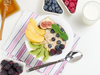 milk, plate with oatmeal porridge and fruit, honey in a bowl on a white table. Healthy breakfast