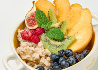boiled oatmeal with fruit in a round plate on a white table, healthy breakfast. View from above