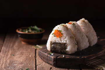 Japanese traditional snack rice balls triangle onigiri with raw salmon and red caviar on a dark wooden board in rustic style