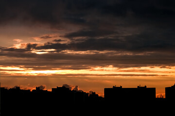 The black silhouette of the city at sunset. Yellow sky with clouds and rays of light breaking through them