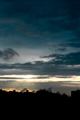 The black silhouette of the city at sunset. Dark blue sky with clouds and rays of light breaking through them on the metropolis