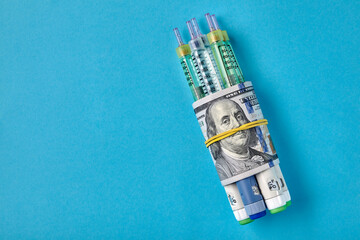 Insulin syringe pens wrapped in dollar bills on a blue background - obrazy, fototapety, plakaty