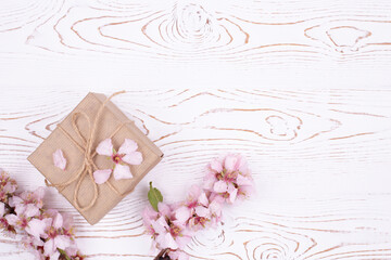 Spring composition gift , wrapped in craft paper, spring blossoming almond branch with flowers on a gray whitewashed rustic wooden table. Flat lay, copy space