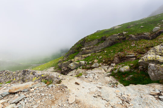 steep slopes of fagaras mountains in fog. huge rocks on grassy hills. travel romania in summer