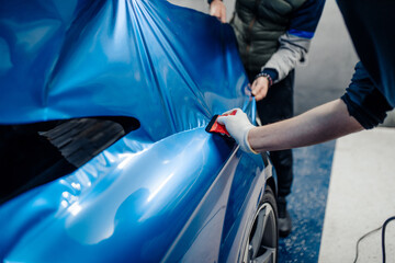 Car wrapping specialists putting vinyl foil or film on car. Selective focus.